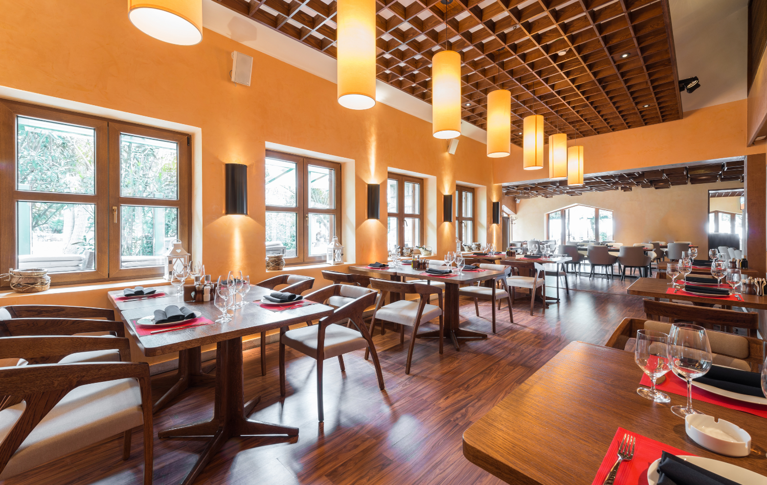 Restaurant dining room with set wooden tables, upholstered chairs, and pendant lighting